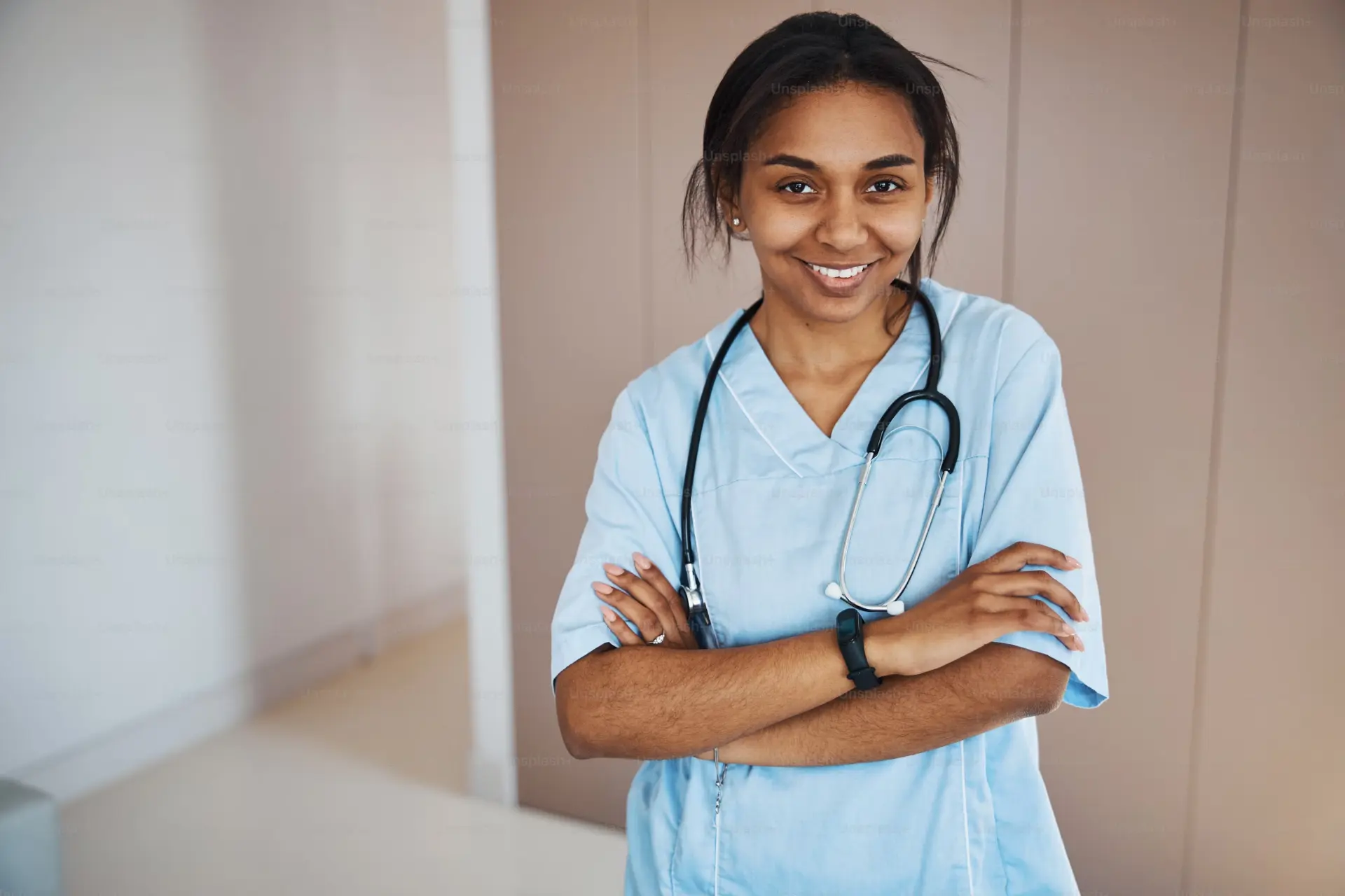 Staff nurse in blue scrubs smiling in a hospital corridor