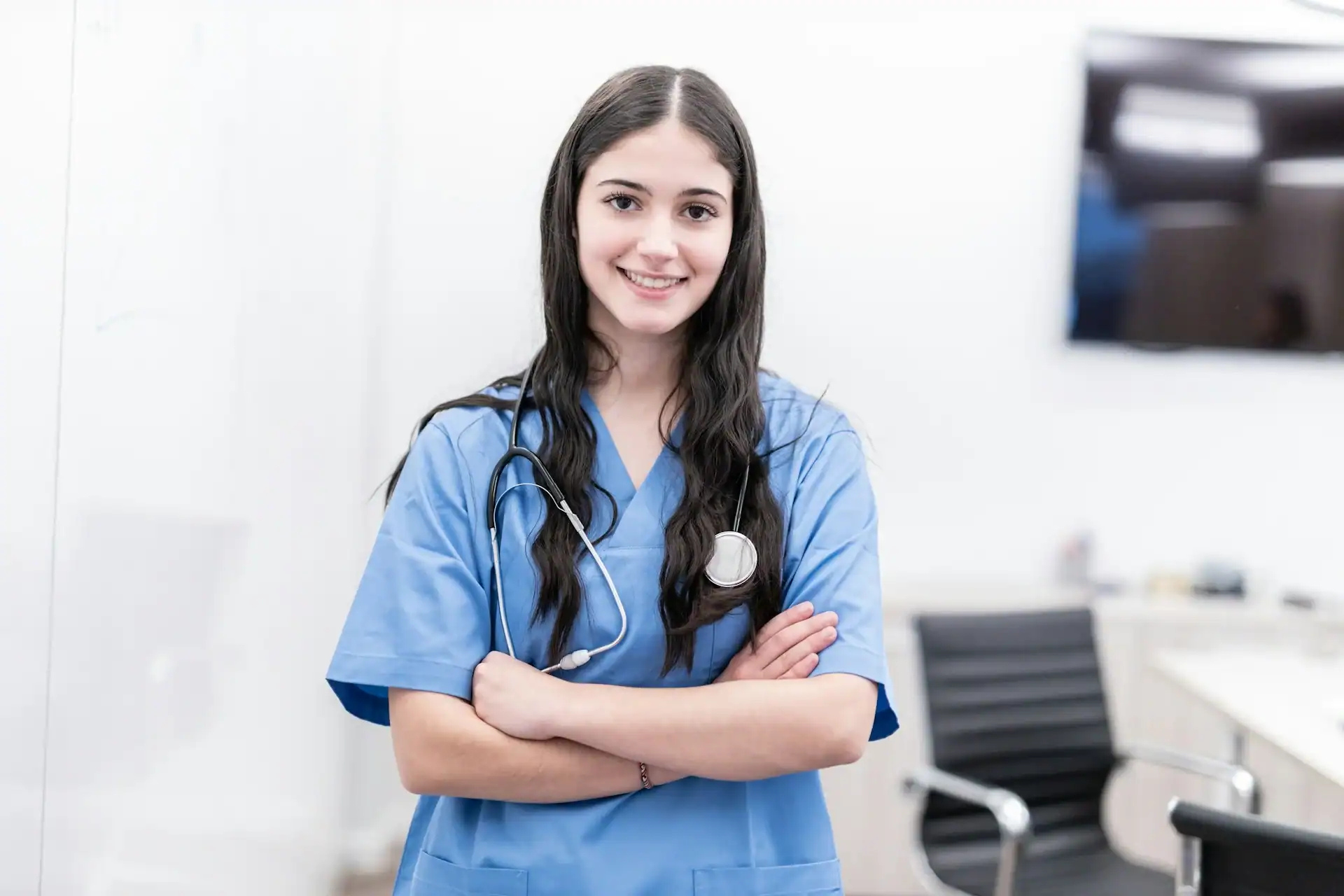 Nurse in blue scrubs with a stethoscope standing in a clinic exam room